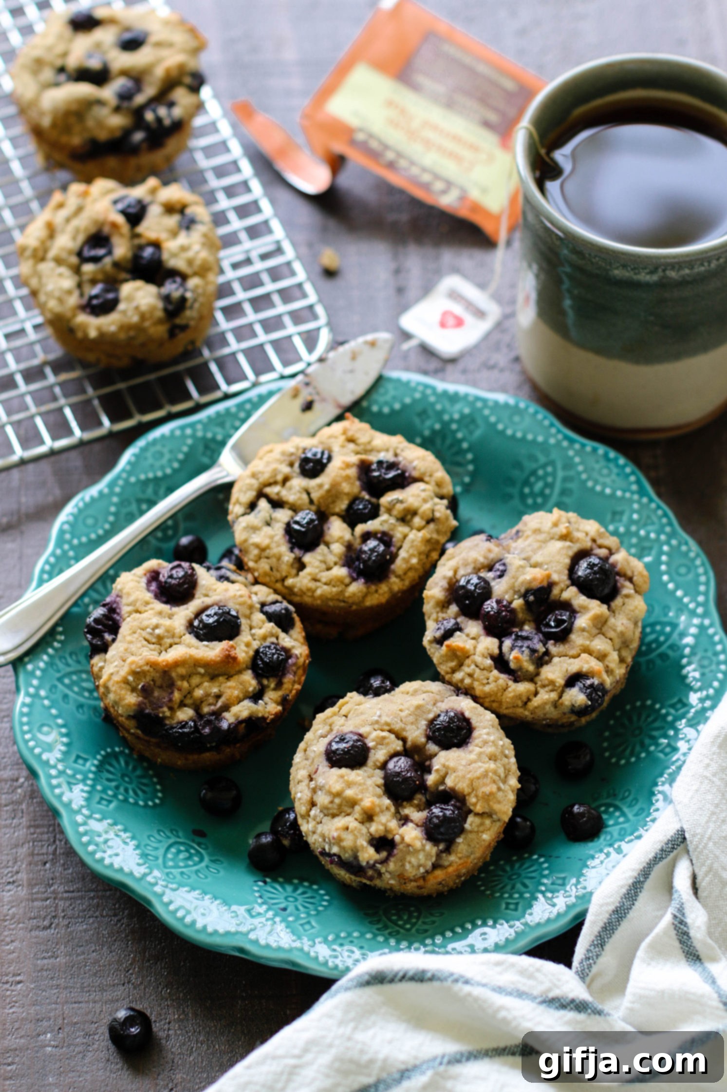 Ultimate Vegan and Gluten-Free Blueberry Muffins 7 The Best Vegan & Gluten Free Blueberry Muffins served on blue plate with a knife on wooden board with mug of tea