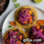 Sweet Potato Black Bean Fiesta Tostadas 8 A top-down view of a single Sweet Potato & Black Bean Tostada on a wooden cutting board, garnished with fresh cilantro and a lime wedge.