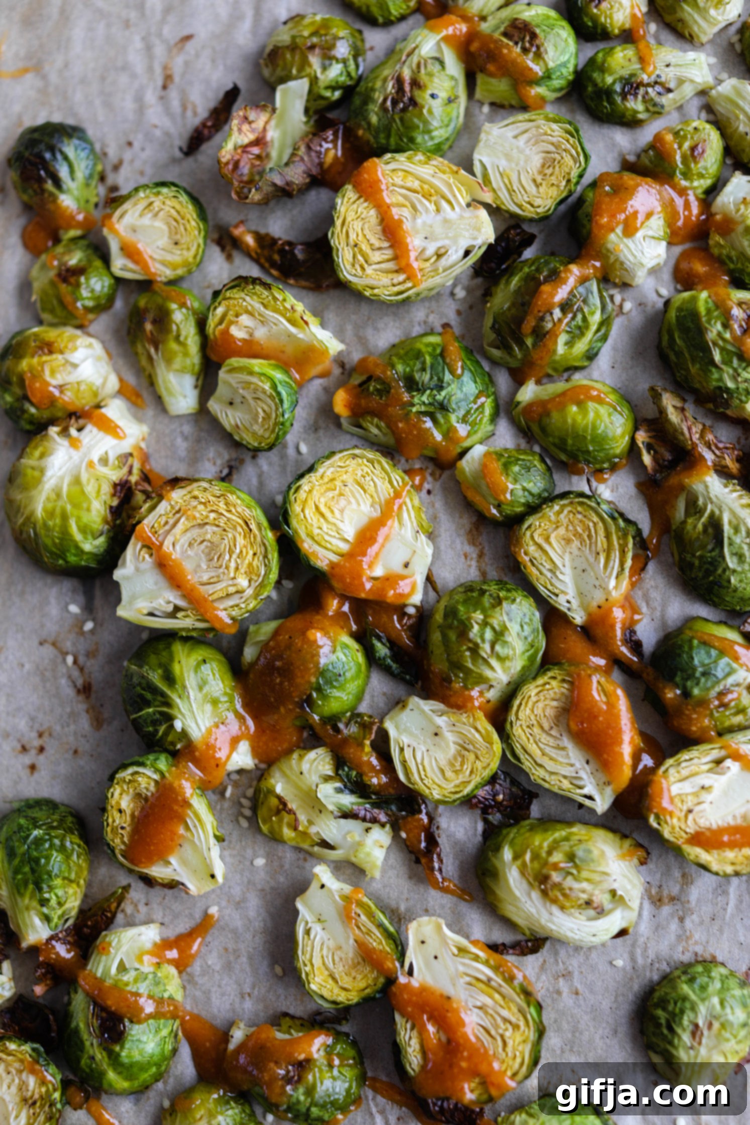 Crispy Roasted Brussels Sprouts with Toasted Hazelnut Butter Sauce 24 Perfectly Roasted Brussels Sprouts with Spicy Hazelnut Butter Sauce, garnished with sesame seeds, on parchment paper.