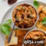 Sun-Dried Tomato and Basil Hummus 10 A bowl of Sun-Dried Tomato and Basil Hummus, garnished with fresh basil leaves and diced sun-dried tomatoes, surrounded by pita chips.
