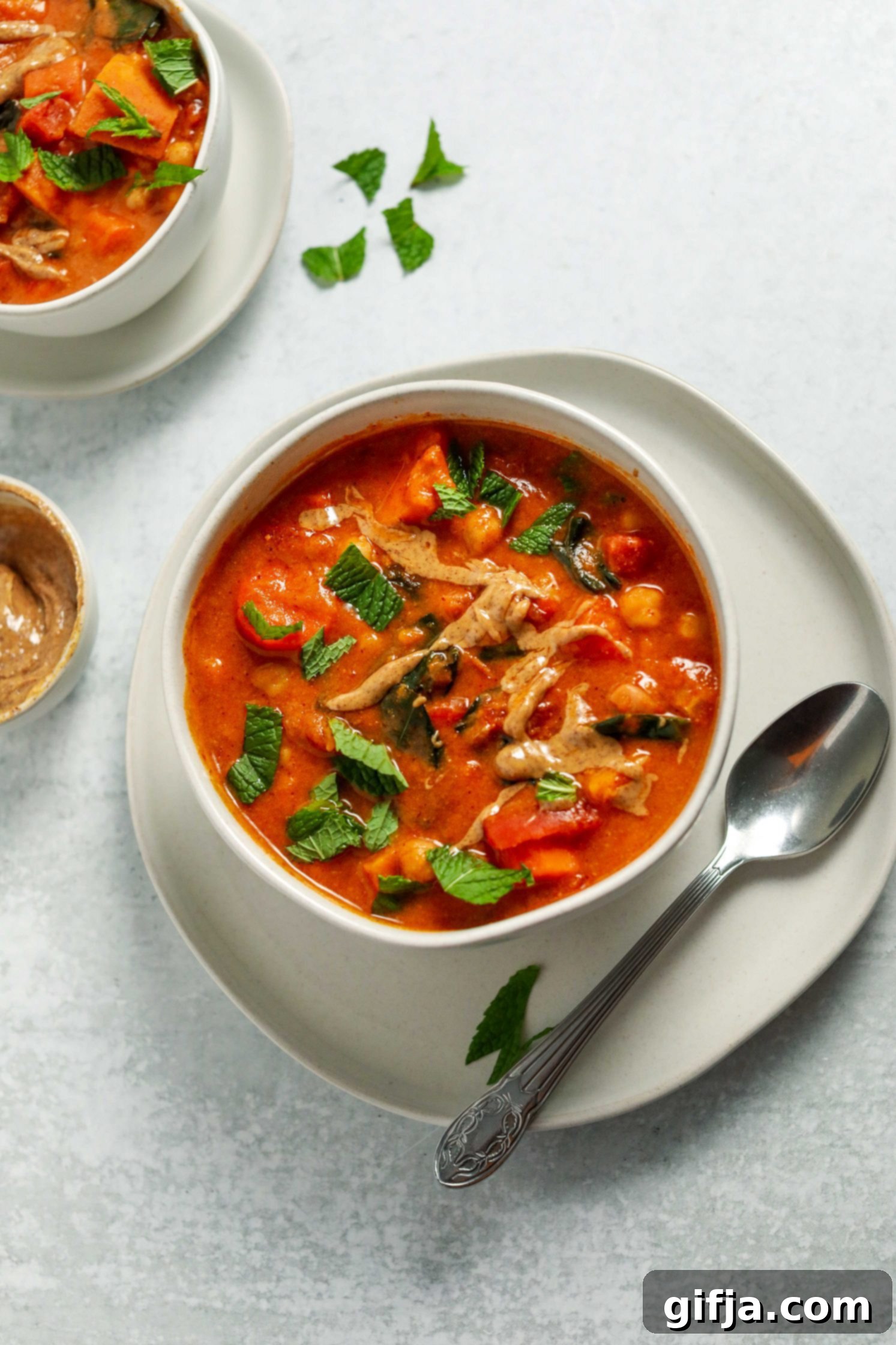 Golden Groundnut Pot 2 African Peanut Butter Stew served in a bowl on a plate with a spoon and fresh mint on top by Flora & Vino