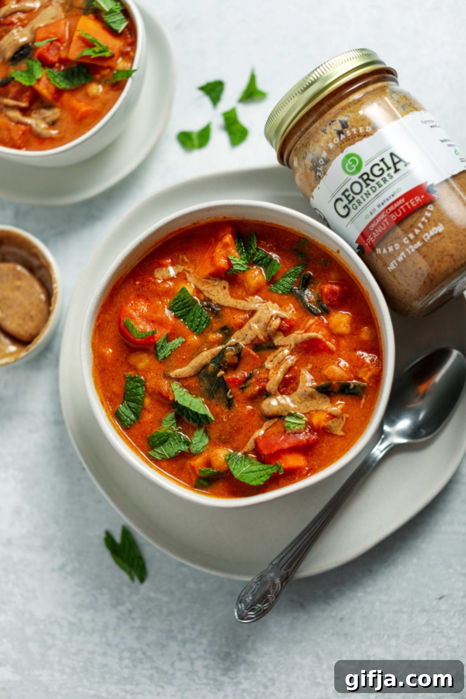 Golden Groundnut Pot 5 African Peanut Butter Stew served in a bowl on a plate with a spoon and fresh mint on top by Flora & Vino