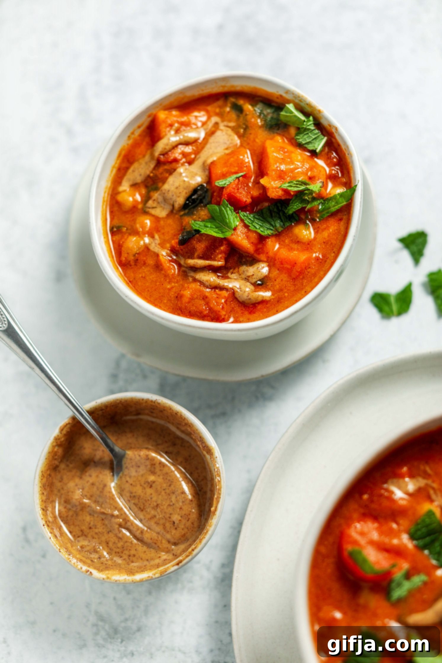 Golden Groundnut Pot 7 African Peanut Butter Stew served in a bowl on a plate with a spoon and fresh mint on top by Flora & Vino