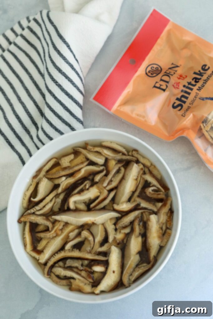 Eden Foods Sliced Dried Shiitake Mushrooms soaking in a bowl of hot water, rehydrating to their plump texture, with a blue and white striped towel on the side, demonstrating the crucial first step.