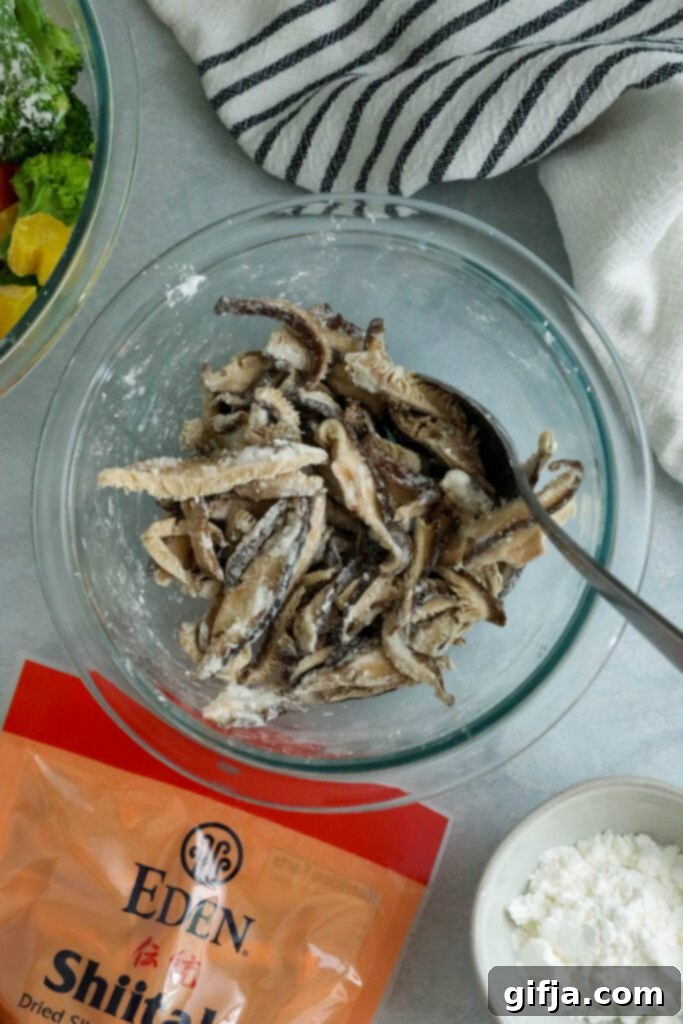 Close-up shot of rehydrated shiitake mushrooms being tossed with cornstarch in a mixing bowl, illustrating the essential step to ensure a crispy texture during stir-frying.