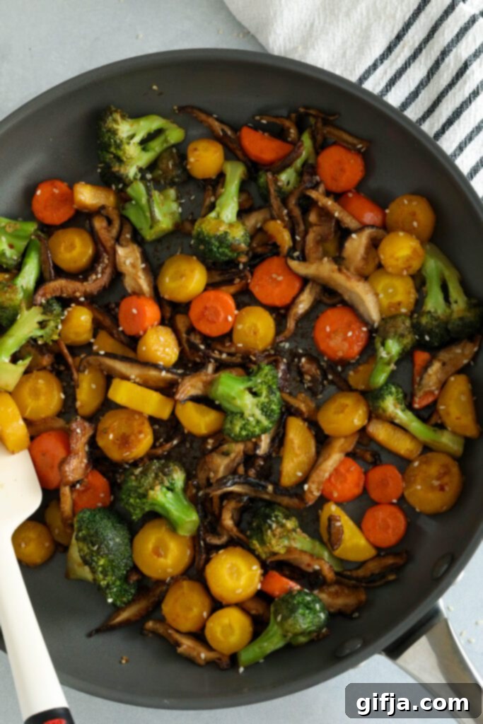 Sesame Shiitake and Broccoli Stir-Fry in a pan, garnished generously with toasted sesame seeds, with a spatula ready to serve and a blue and white striped towel in the corner – a perfect vegan stir-fry by Flora & Vino.