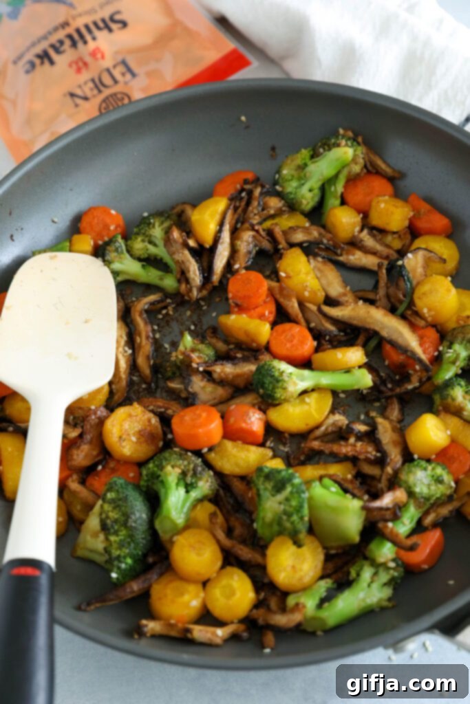 Sesame Shiitake and Broccoli Stir-Fry in a pan being tossed with a spatula, coated in a sticky, savory sauce, ready to be served – a delicious vegan meal by Flora & Vino.