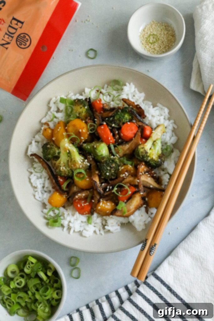 A beautifully plated Sesame Shiitake & Broccoli Stir-Fry served over jasmine rice, garnished with vibrant green onions and toasted sesame seeds, with elegant chopsticks on the side, highlighting a complete vegan meal by Flora & Vino.