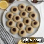 Sun-Kissed Almond Thumbprint Gems 18 A plate of freshly baked Lemon Almond Flour Thumbprint Cookies with berry jam centers, surrounded by lemon halves, on a blue and white striped towel.