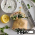 Greek Salad Wrap 14 Chopped Greek Wrap sliced in half served with bowl of Tzatziki Sauce on plate with lemon and dill and parsley