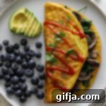 Fluffy Vegan Mushroom Omelette 12 Vegan Mushroom Omelette on a plate with blueberries and avocado, topped with hot sauce and cilantro