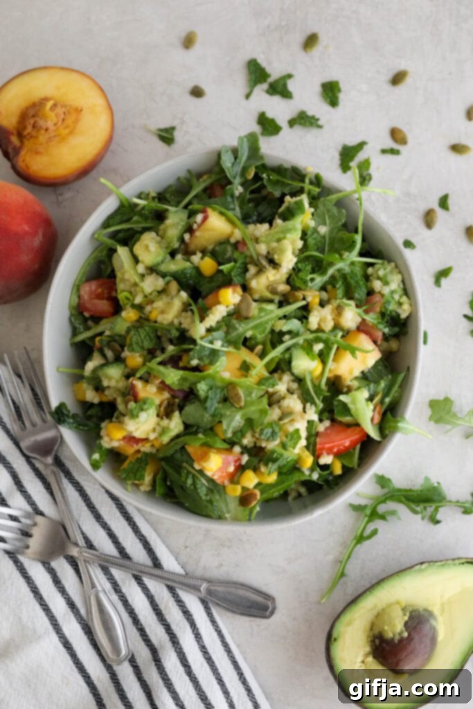 Vibrant Summer Harvest Millet Bowl, brimming with fresh peaches, avocado, arugula, and a sprinkle of pumpkin seeds. Served with a striped towel and two forks, ready to be enjoyed.