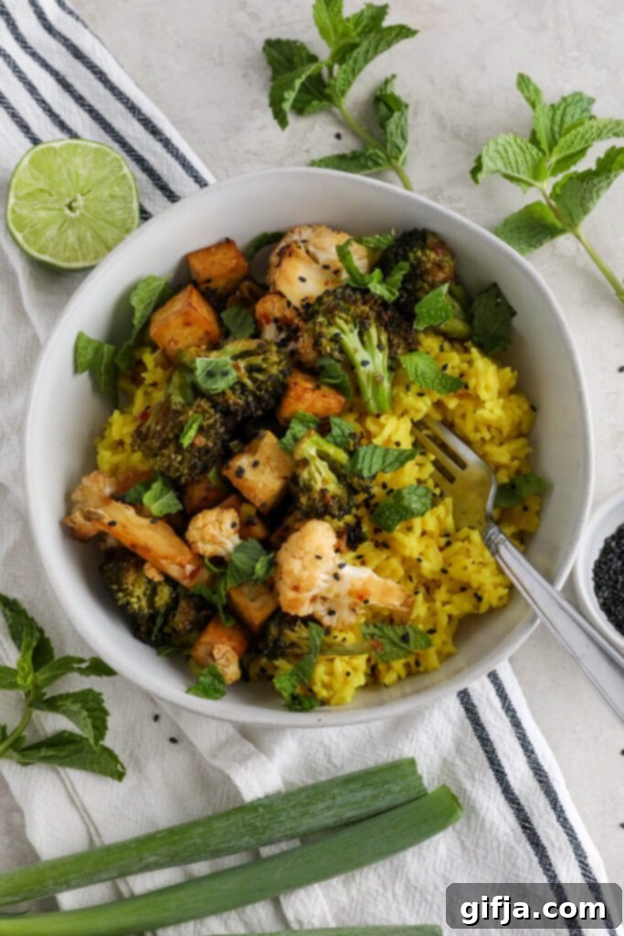 A beautifully plated Coconut Curry Rice Bowl with vibrant yellow rice, green broccoli, white cauliflower, and golden-brown tofu, garnished with fresh herbs.