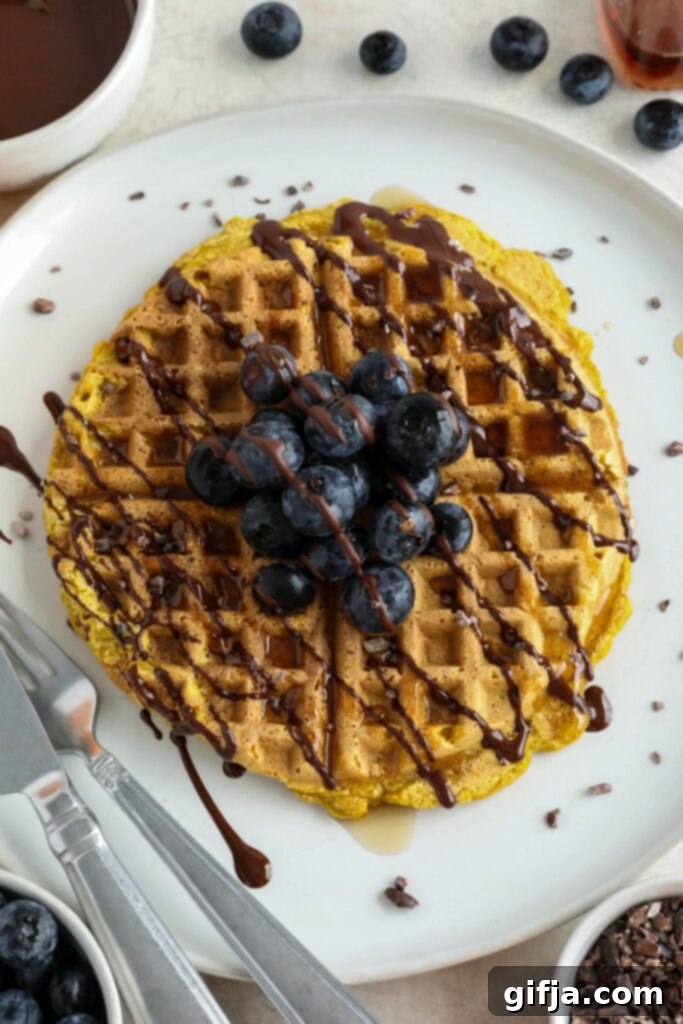 Delicious Pumpkin Turmeric Waffles adorned with fresh blueberries, crunchy cacao nibs, and a rich chocolate drizzle, served on a white plate, ready for a healthy and satisfying breakfast