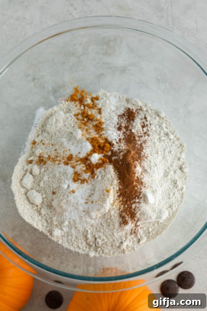 Dry ingredients for pumpkin turmeric waffles, including gluten-free rolled oats, baking powder, and ground cinnamon, measured in a bowl, before blending into a fine flour