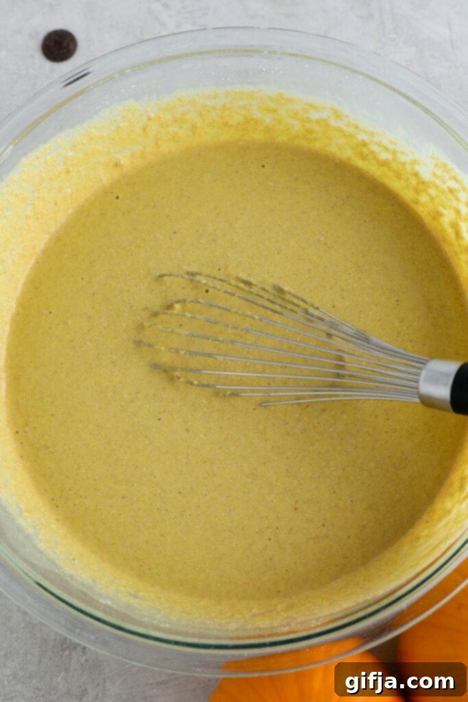 Smooth, golden pumpkin turmeric waffle batter in a mixing bowl, ready to be cooked into delicious waffles, with a whisk nearby