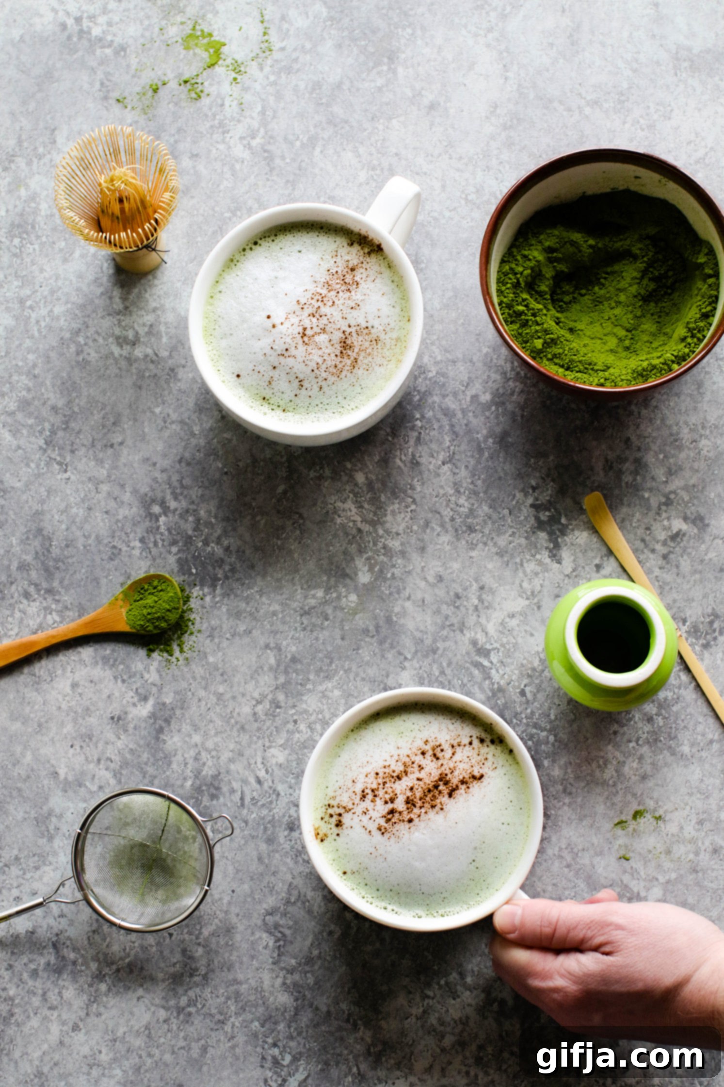 Cinnamon Almond Matcha Latte served in mugs with hand grabbing one by Flora & Vino