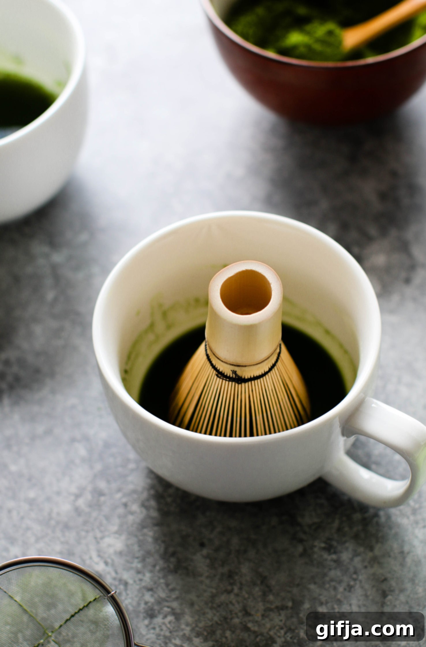 matcha whisker in mug with matcha powder in background by Flora & Vino