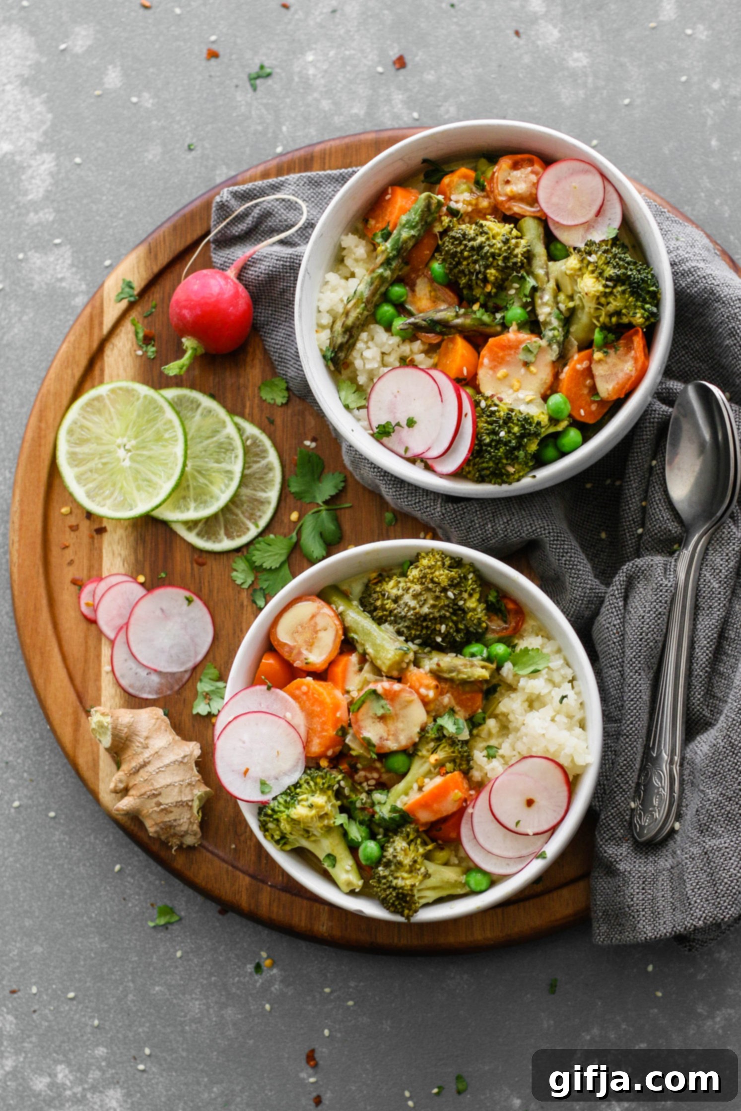 Vibrant Green Coconut Curry with Cauliflower Rice 2 Green Coconut Curry with Cauliflower Rice served on wooden circle board with fresh lime, sliced radish, cilantro, and two spoons on the side