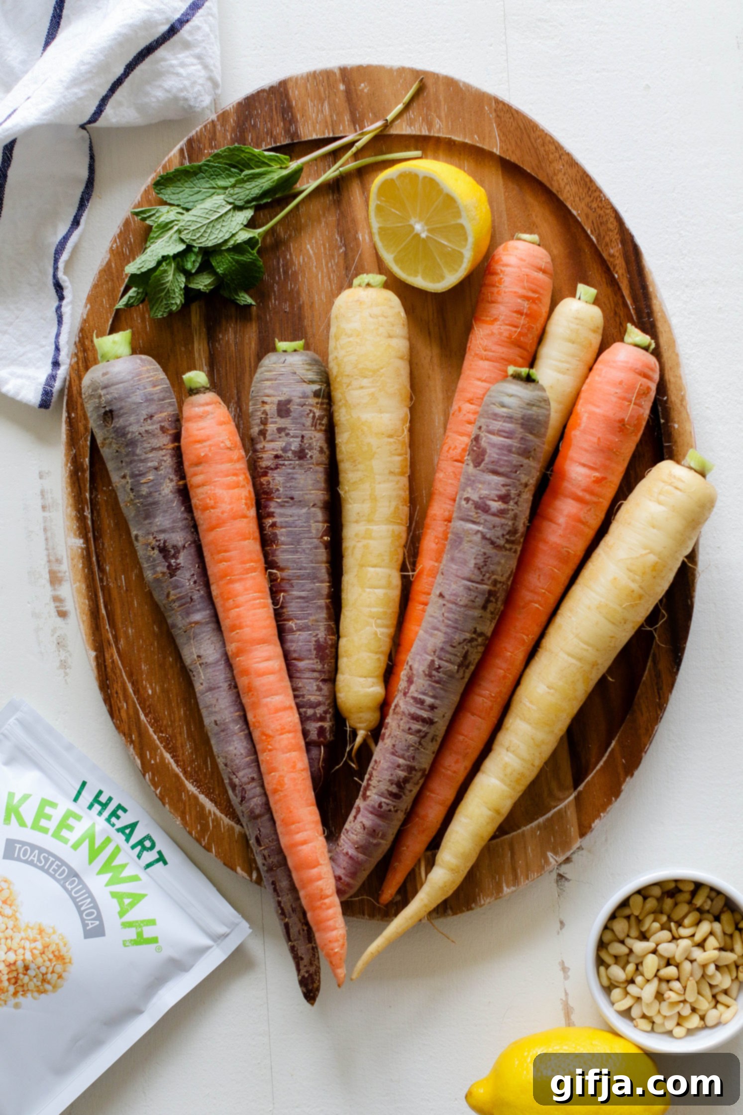 Vibrant Roasted Carrots 3 rainbow carrots on wooden board with lemon and fresh mint with pine nuts and white and blue striped towel on the side