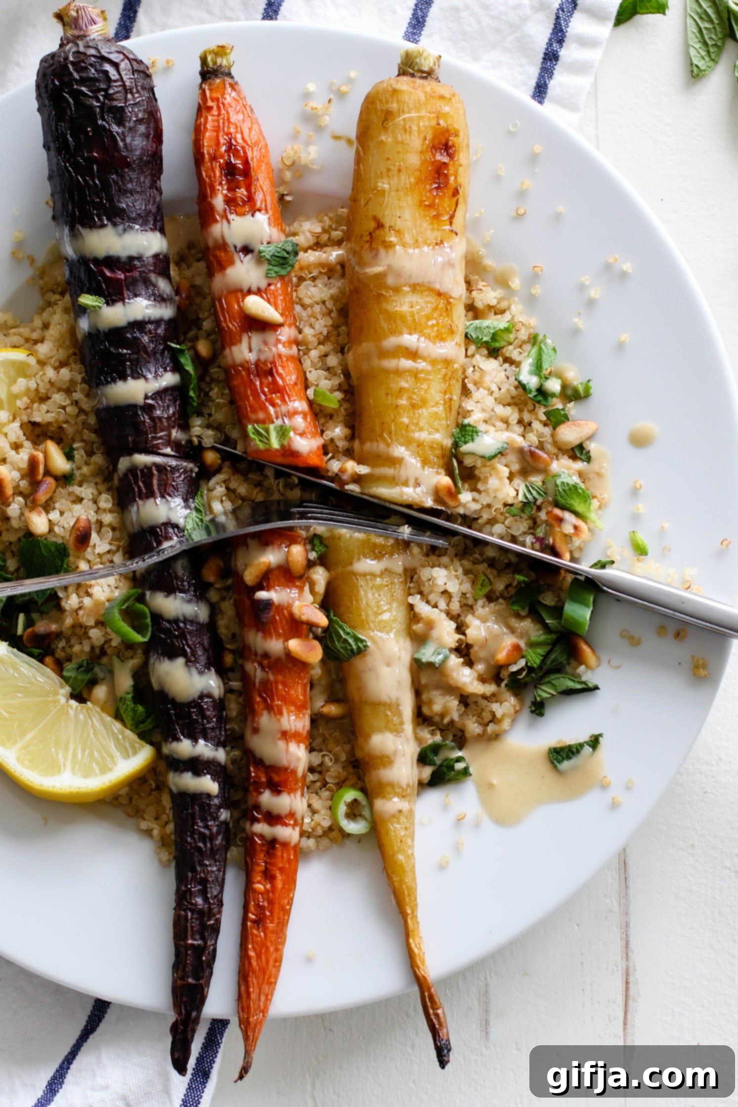 Vibrant Roasted Carrots 9 Rainbow Roasted Carrots served on plates over quinoa with fresh lemon, shredded mint, toasted pine nuts, and drizzle of tahini with fork and knife cutting into carrots