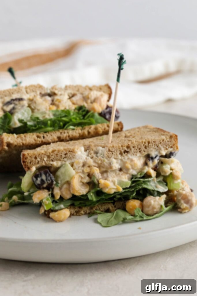 Halved Cranberry Chickpea Salad Sandwich on a white plate with a fork, ready to eat