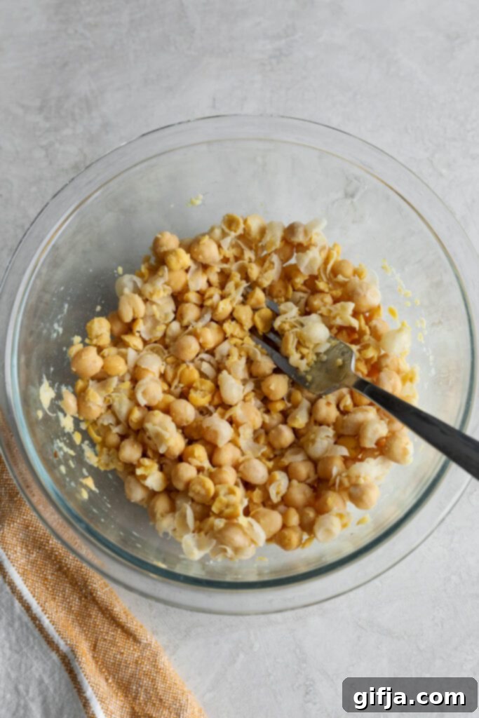 Smashed chickpeas in a glass bowl with a fork, ready for mixing