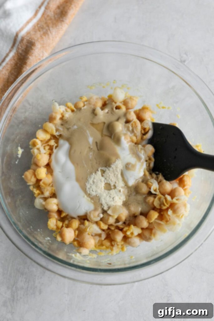Wet dressing ingredients being added to the smashed chickpeas in a bowl