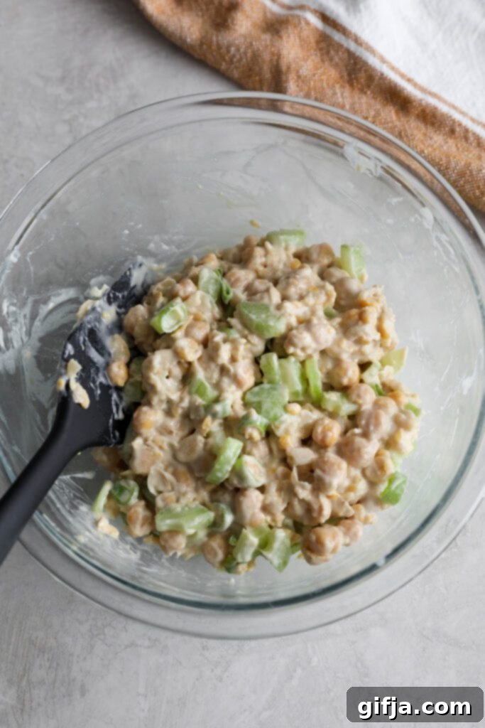 Fully mixed cranberry chickpea salad in a clear glass bowl with a spatula