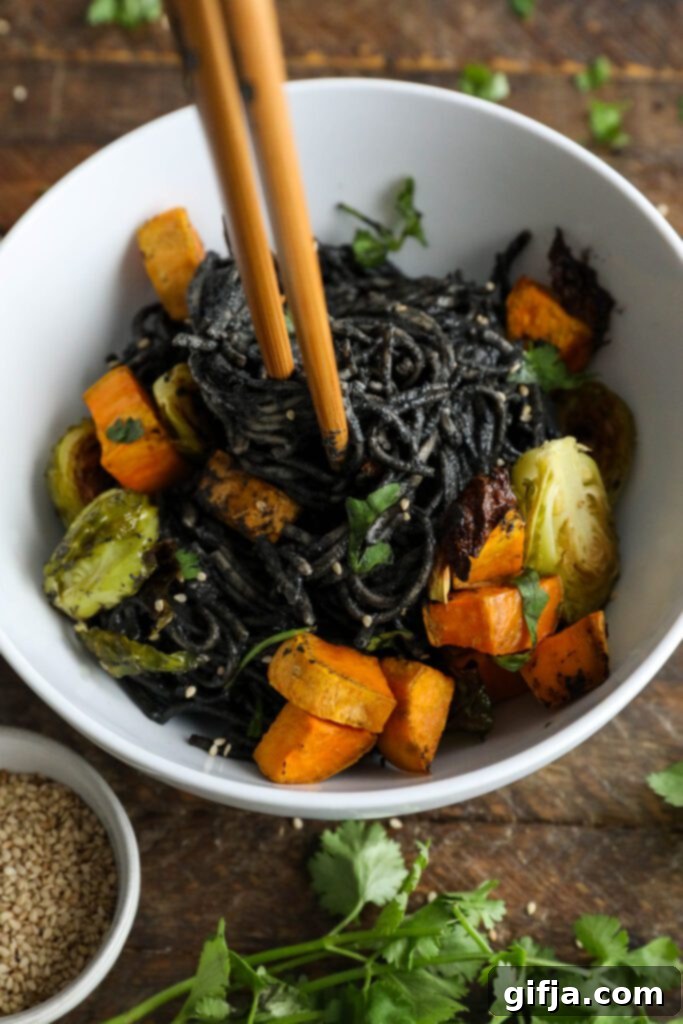 Midnight Sesame Noodle Bowl 12 Black Sesame Noodle Bowl served in a bowl, garnished with cilantro and sesame seeds, with chopsticks poised to enjoy.