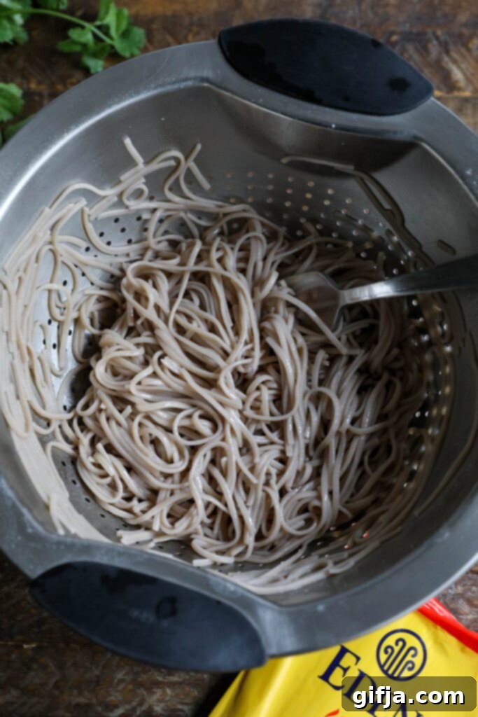 Midnight Sesame Noodle Bowl 6 Buckwheat soba noodles in a colander with a fork, ready to be tossed with sauce.