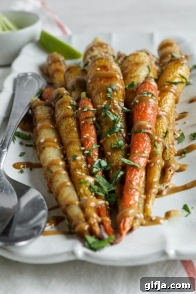 Rainbow Roasted Carrots with SunButter Sauce served on rectangular platter with fork and spoon topped with lime and cilantro and sesame seeds
