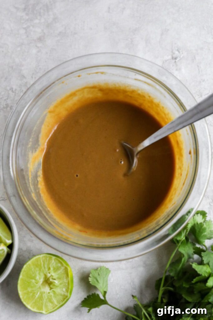 SunButter sauce mixed in glass bowl with spoon surrounded by lime and cilantro 