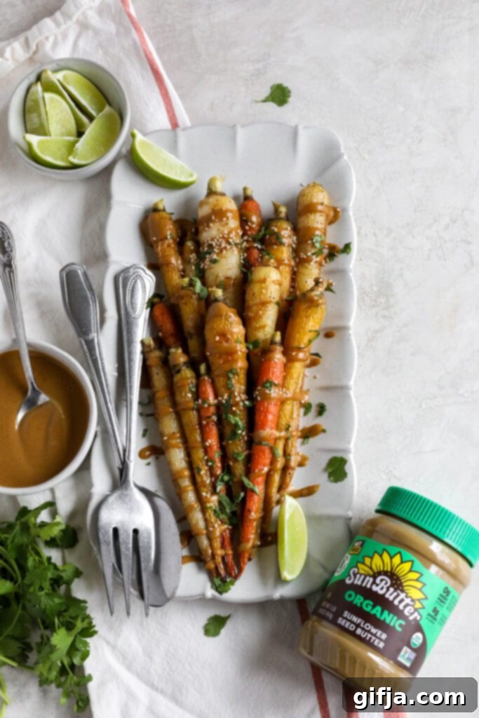 Rainbow Roasted Carrots with SunButter Sauce served on rectangular platter with fork and spoon topped with lime and cilantro and sesame seeds